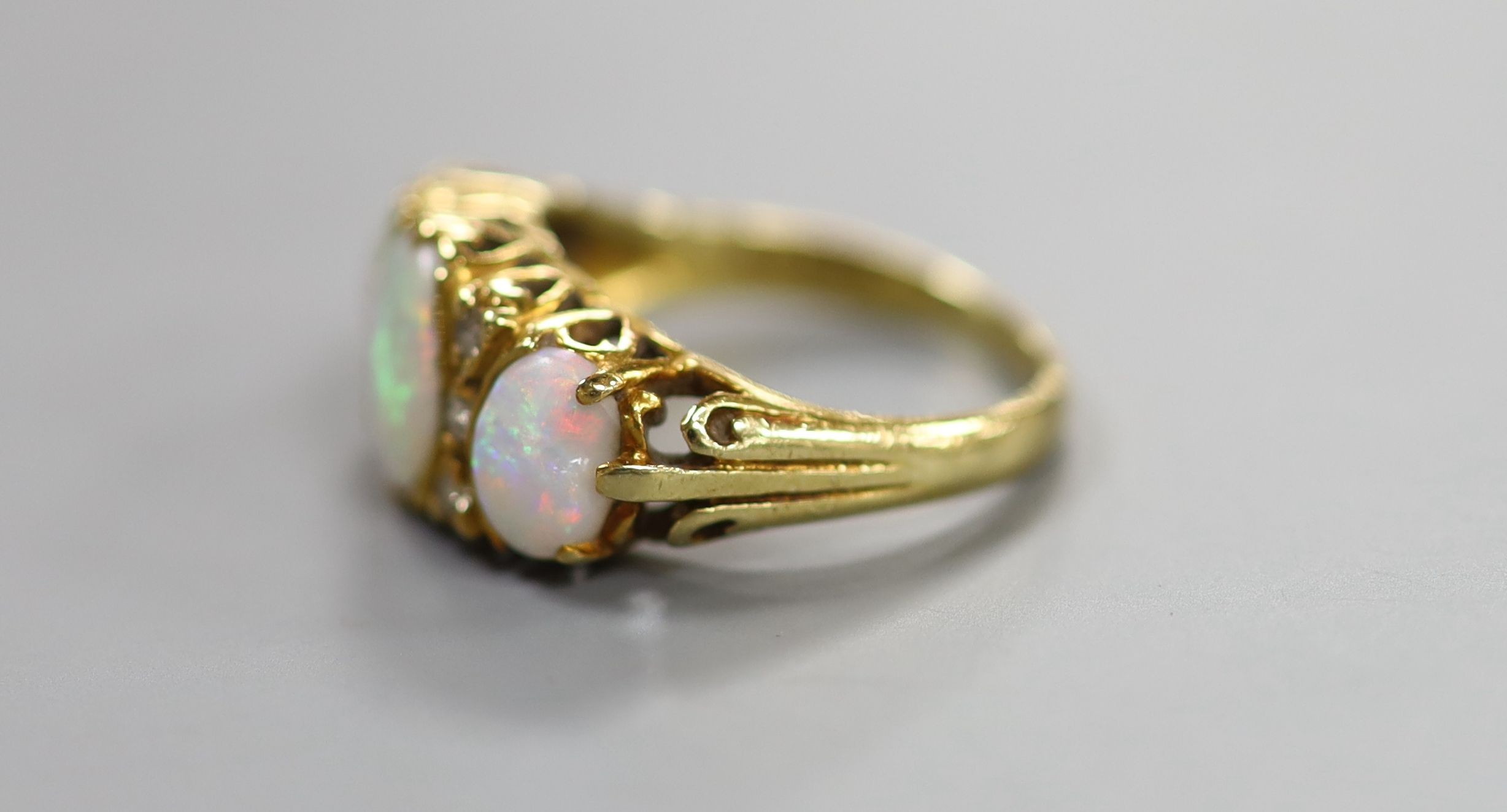 A 1970's Victorian style 18ct gold and graduated three stone white opal half hoop ring, with diamond chip spacers, size N, gross weight 5.9 grams.